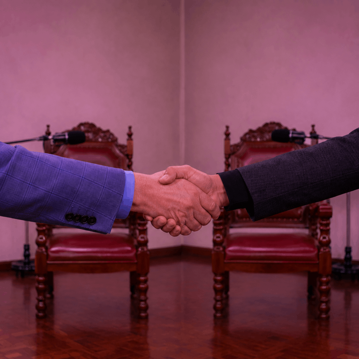 Dos participantes se saludan frente a dos micrófonos y sillas preparadas para grabar